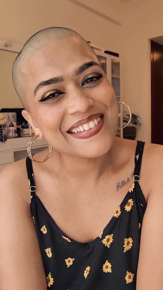 Woman with a closely buzzed haircut smiling in a black floral top