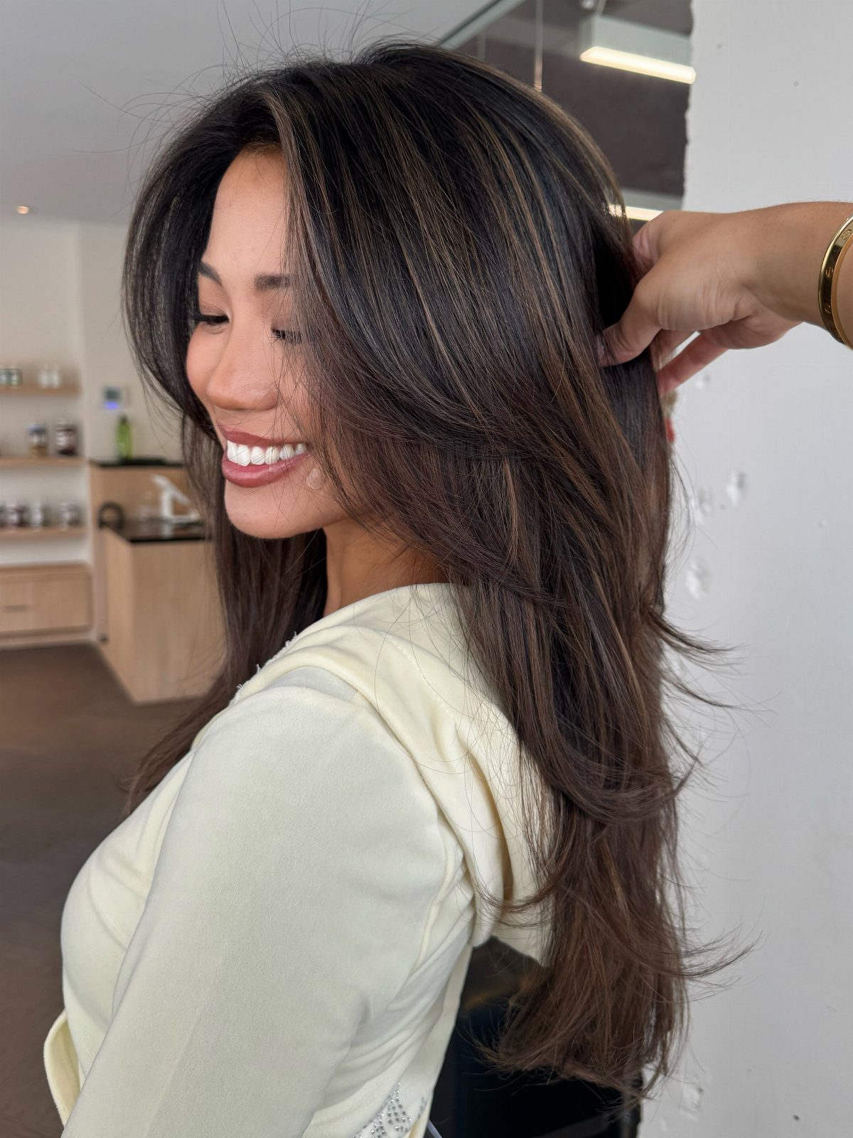 Long dark hair with caramel highlights, a side part, and loose curls