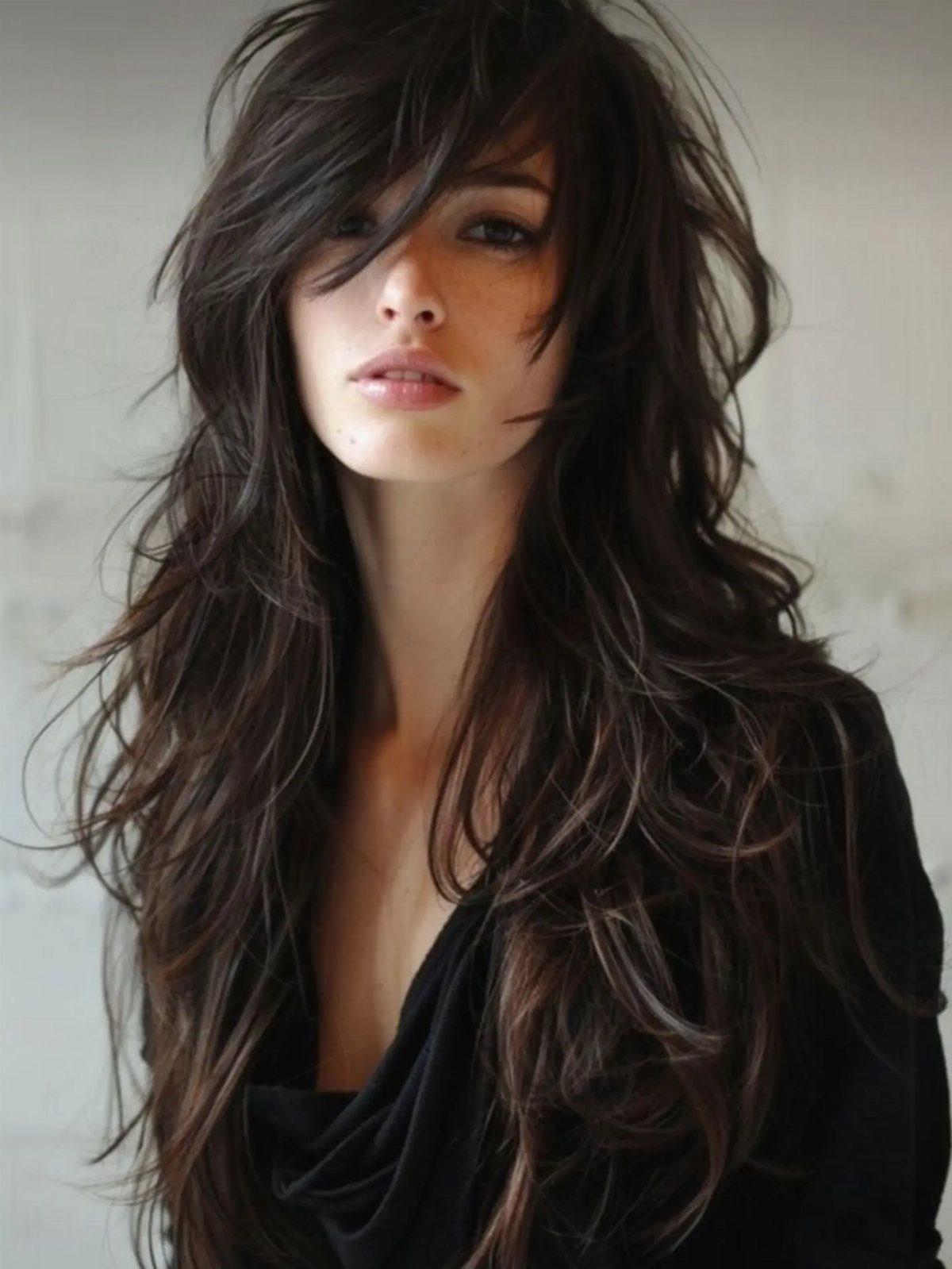 Woman with long dark shag haircut, choppy layers, and sweeping bangs