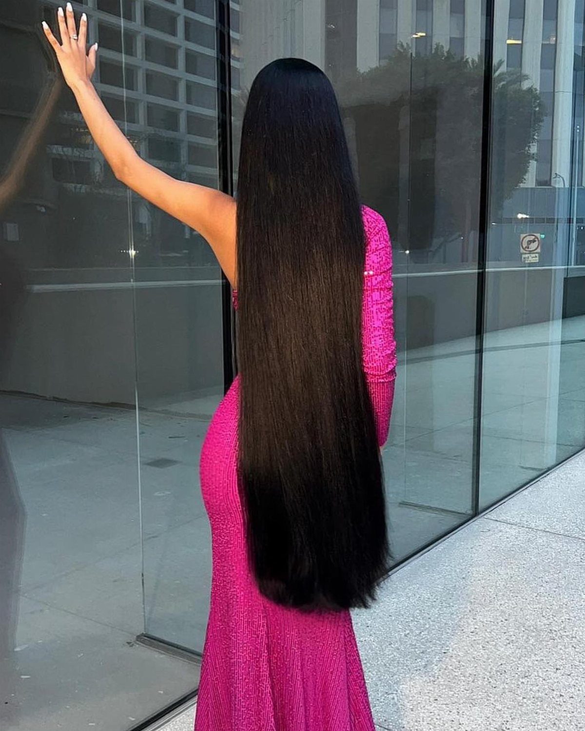 Very long, glossy straight black hair falls down the back of a person in pink