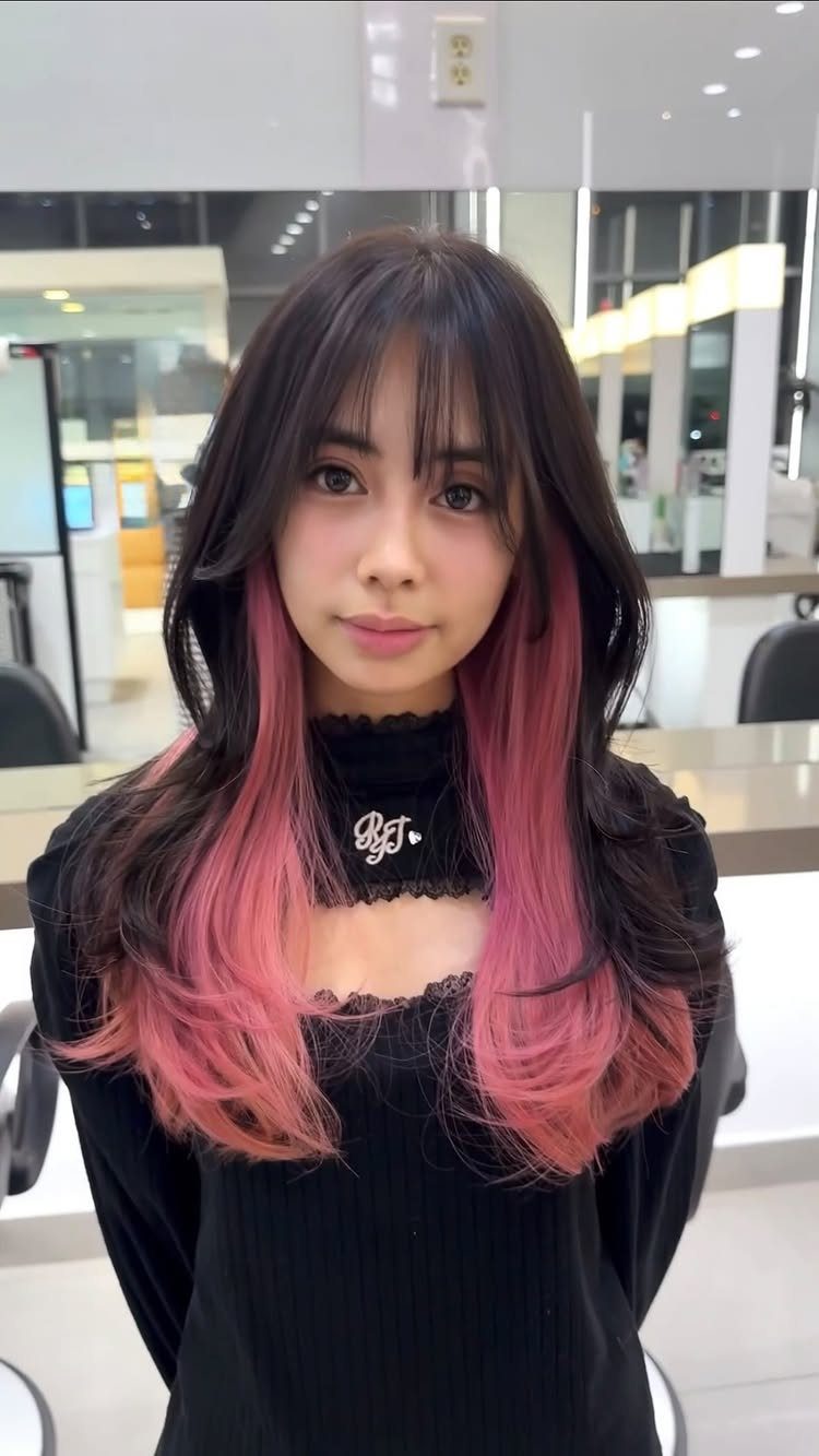 Woman with brown bangs and pink peekaboo underlayers curled at the ends