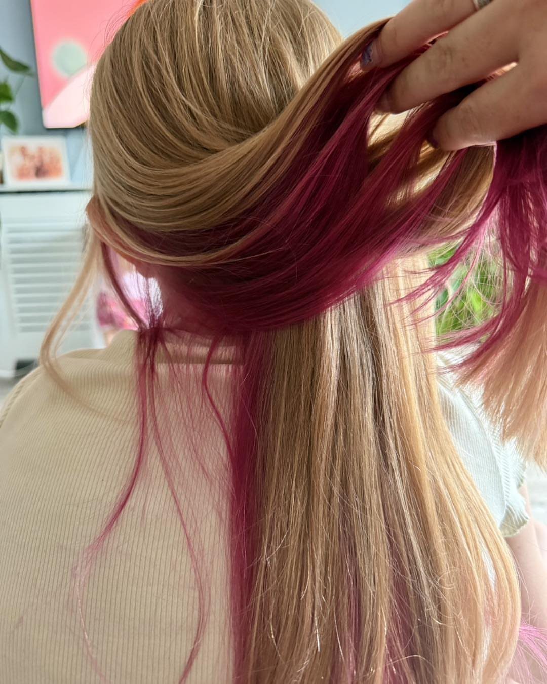 Lifted blonde-brown hair reveals vivid pink underlayers beneath the top strands