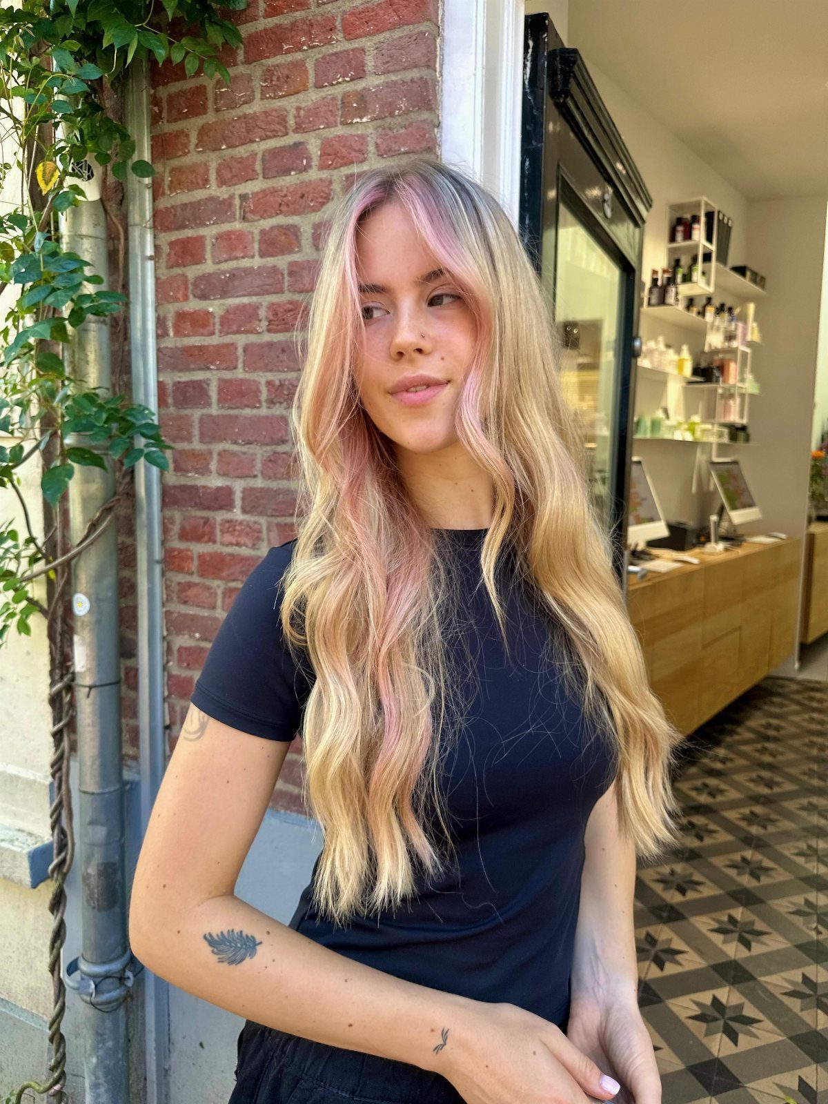 Woman with long blonde waves and pale pink face-framing streaks beside a salon