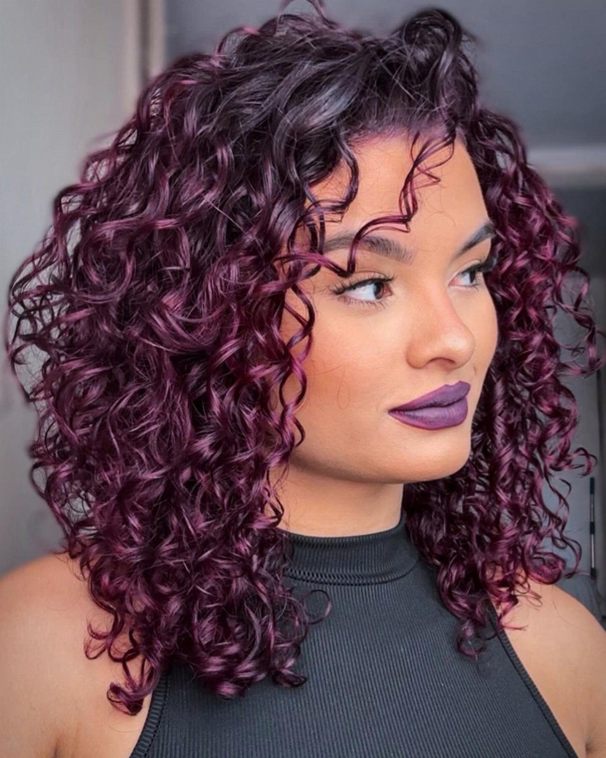 Woman with voluminous plum-purple curls wearing a black sleeveless top