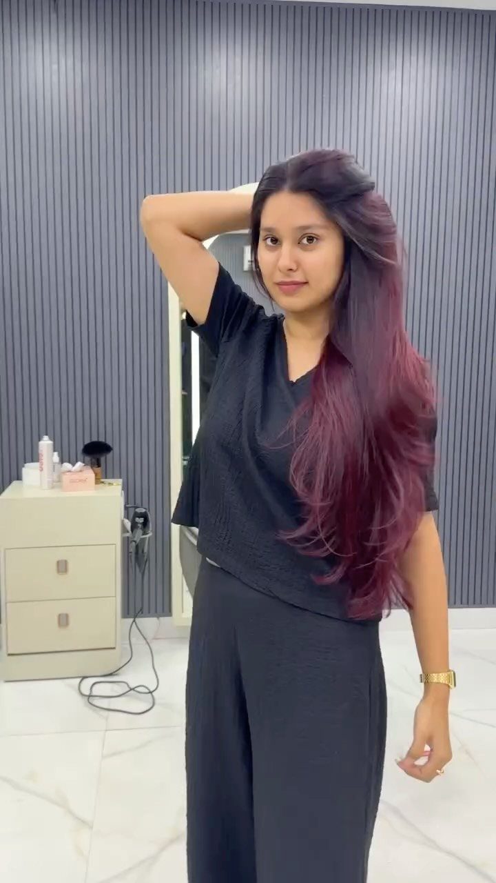 Woman posing in a salon with long, dark-rooted plum-purple hair