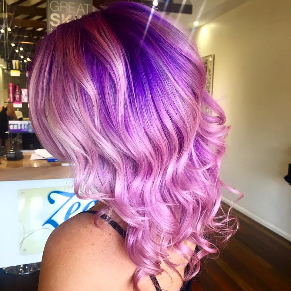 Curled hair fades from deep plum roots into pale lavender pink ends
