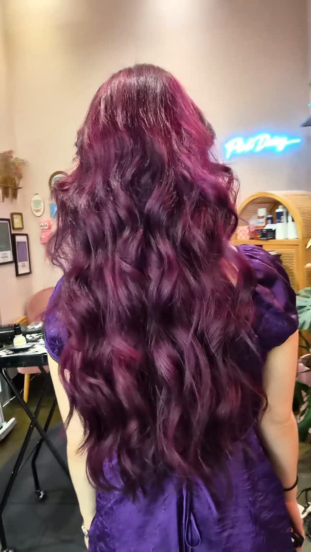 Long wavy hair blends deep plum, magenta, and violet shades in a salon.
