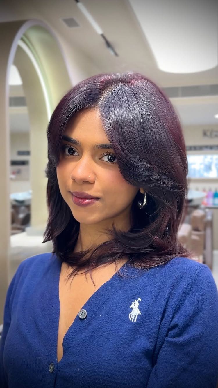 Woman with layered plum-brown hair wearing a blue cardigan indoors