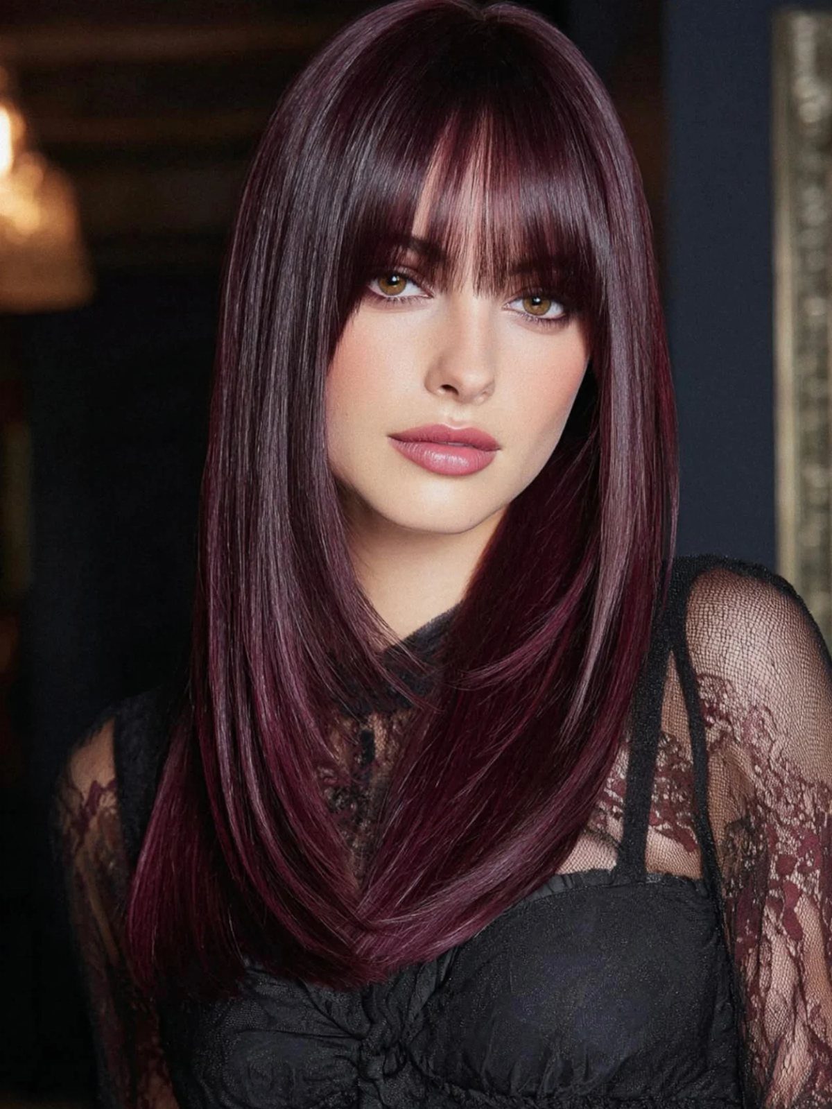 Woman with long plum-burgundy hair and blunt bangs wearing a black lace top