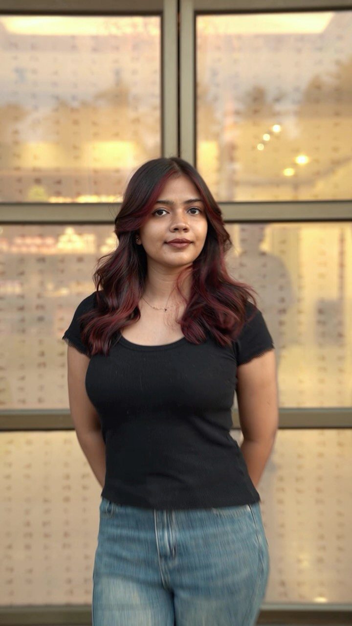 Woman showing wavy brown hair with plum highlights against illuminated display panels