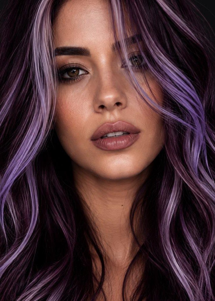 Woman with long wavy dark plum hair and violet highlights against a dark background