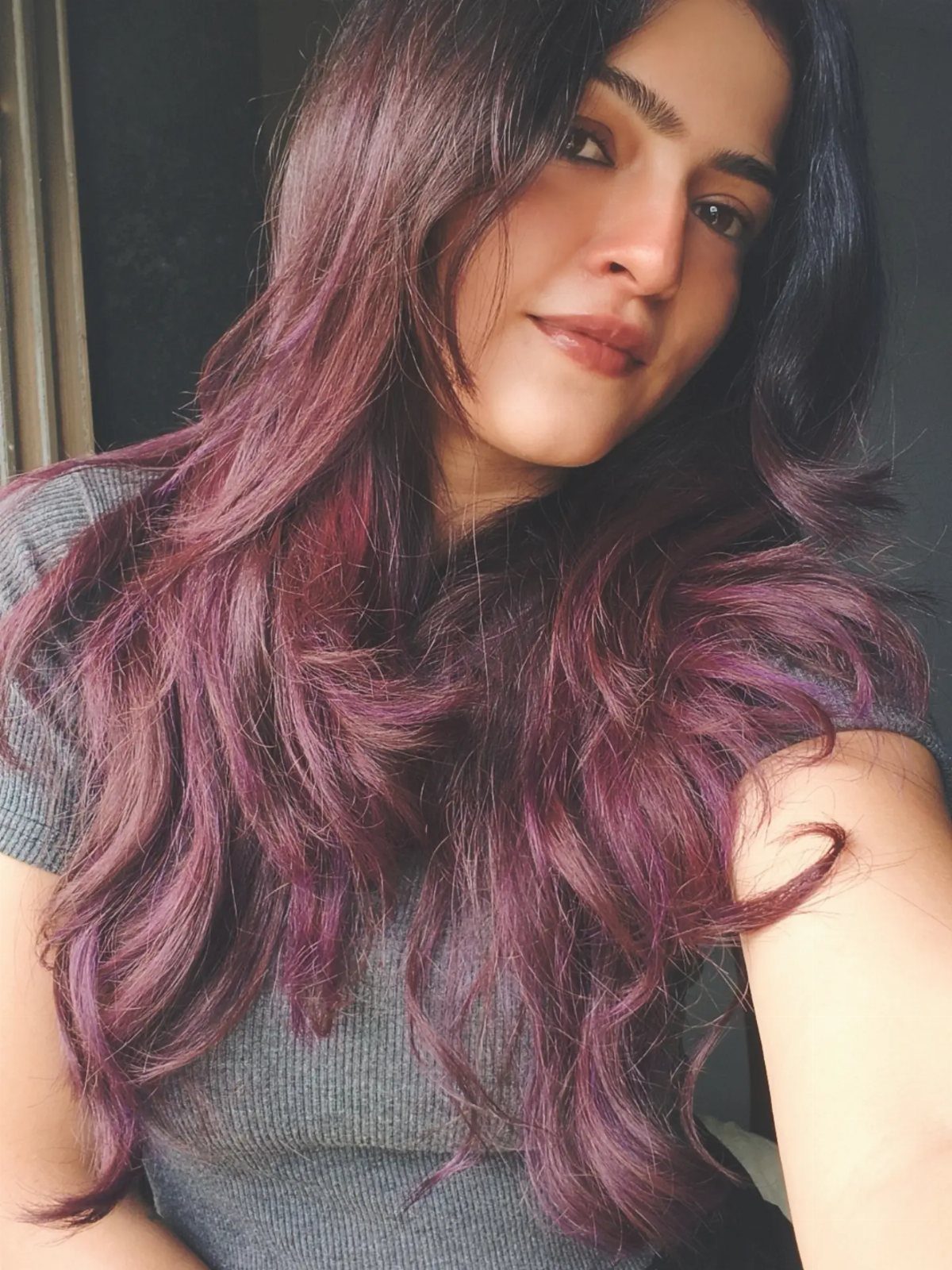 Woman with long wavy dark hair showing a muted plum tint