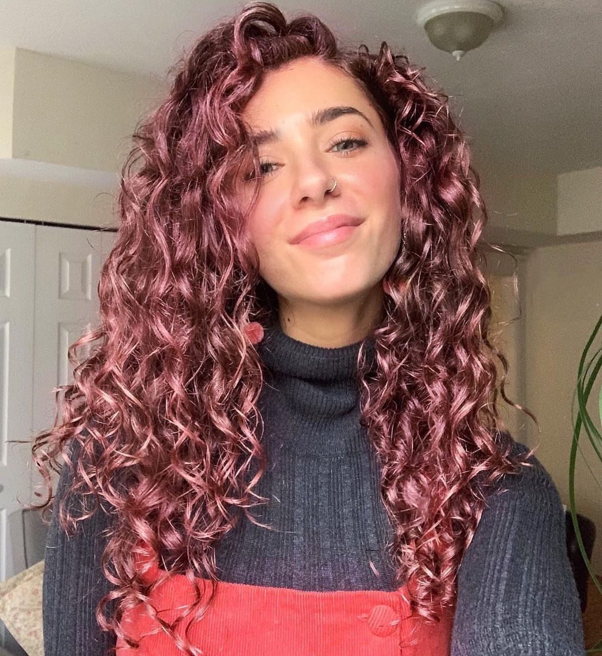 Woman with long blush rose curls and dark roots wearing a dark top
