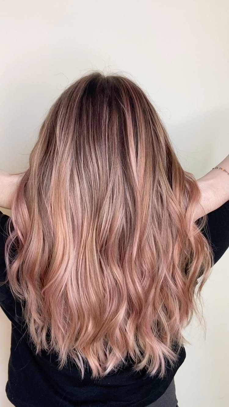 Long wavy hair fades from dark roots through blonde into pale pink ends