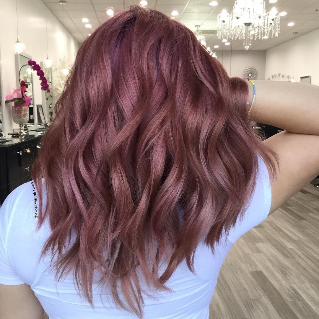 Shoulder-length dusty rose curls with darker roots in a bright salon