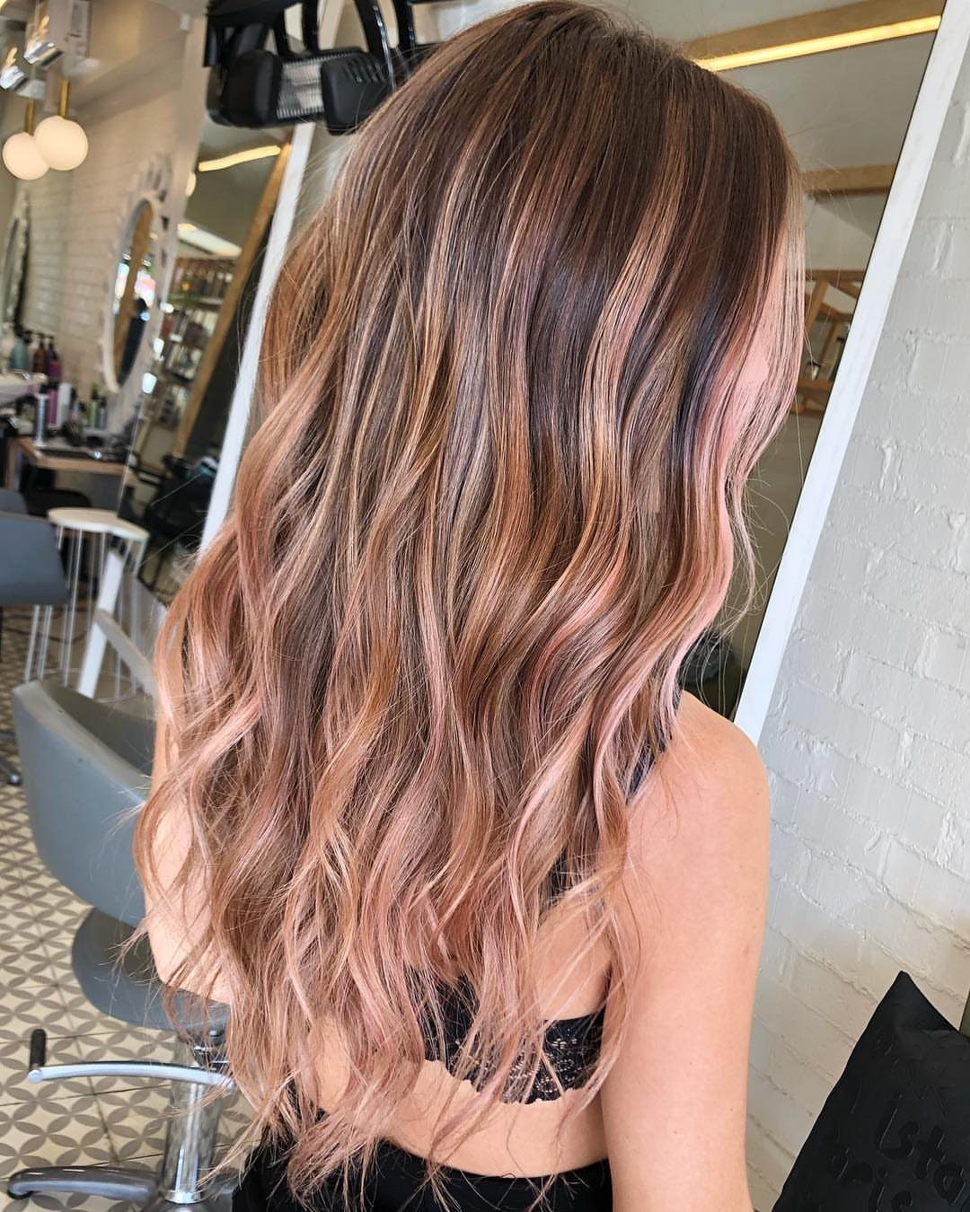 Long wavy blonde hair with pale pink rose-gold streaks in a salon
