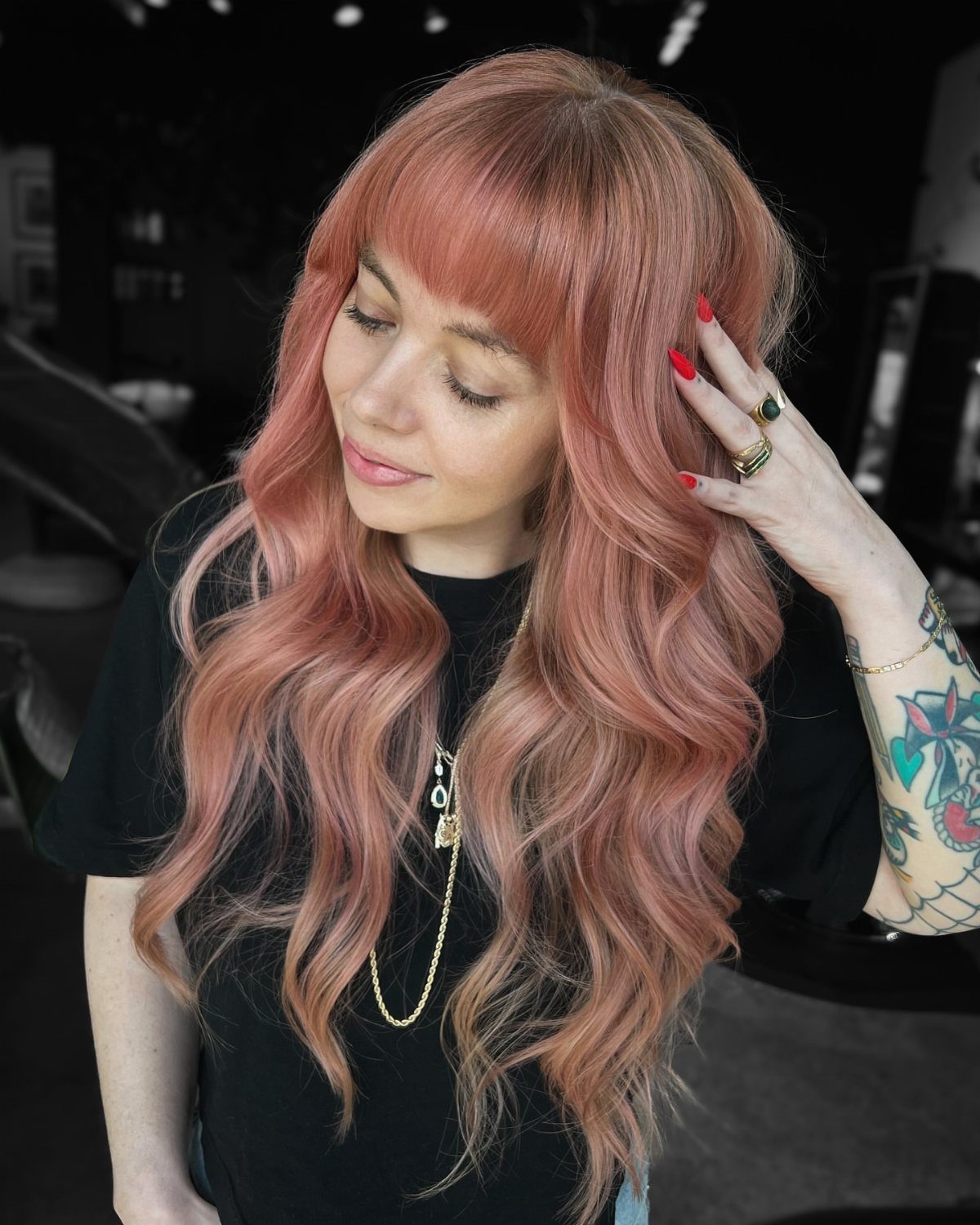Woman with long rose-gold waves and bangs touching her hair