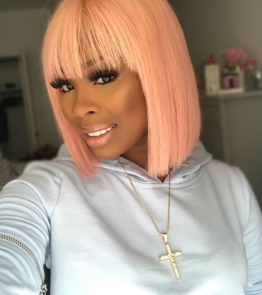 Woman wearing a peachy rose-gold bob wig with blunt bangs