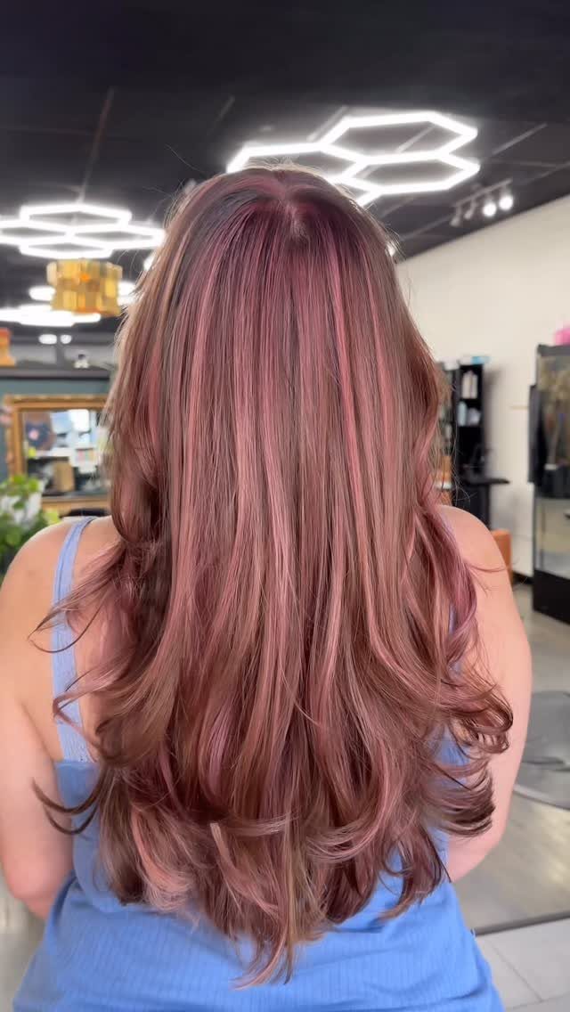 Long layered brunette hair with rose-gold highlights and a center part