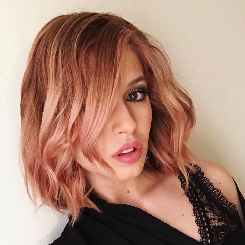 Woman posing with a layered rose-gold bob, dark roots, and loose waves