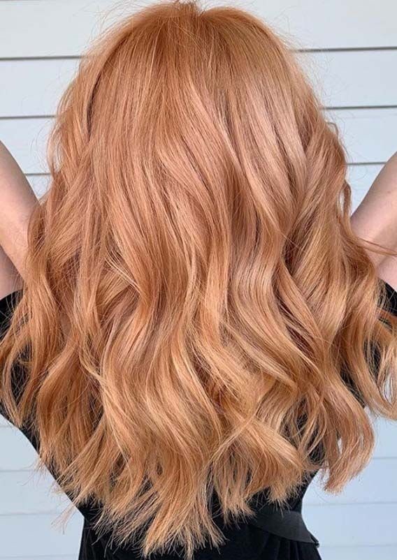 Apricot rose-gold waves fall to the shoulders against a white paneled wall