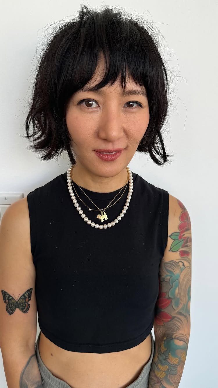 Woman displaying a choppy black bob with uneven bangs and layered necklaces
