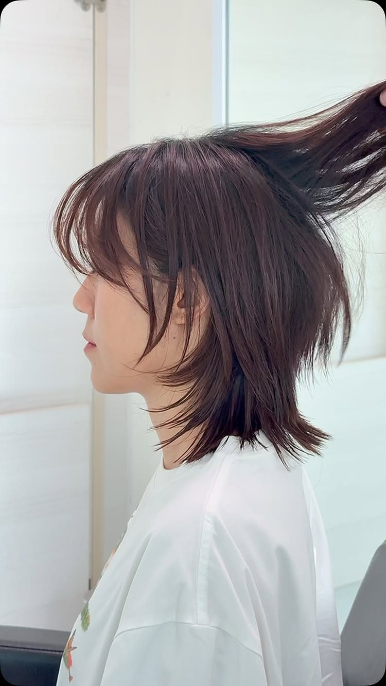 Short choppy layered bob with wispy bangs as a stylist lifts the hair