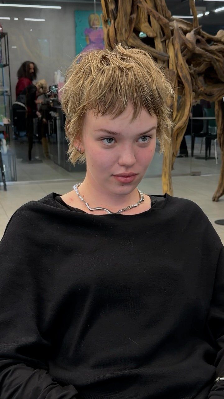 Short layered blonde pixie haircut with textured bangs in a salon