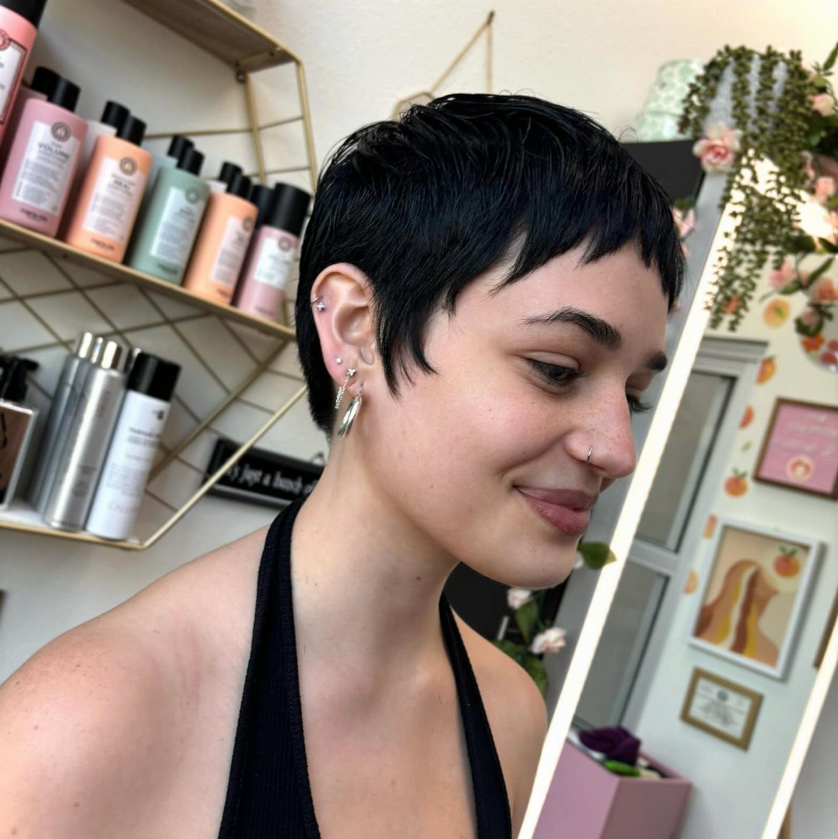 Short dark pixie with choppy microbangs, shown in profile in a salon