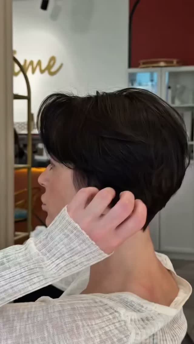 Side-swept pixie with dark layered hair and a tapered nape in a salon