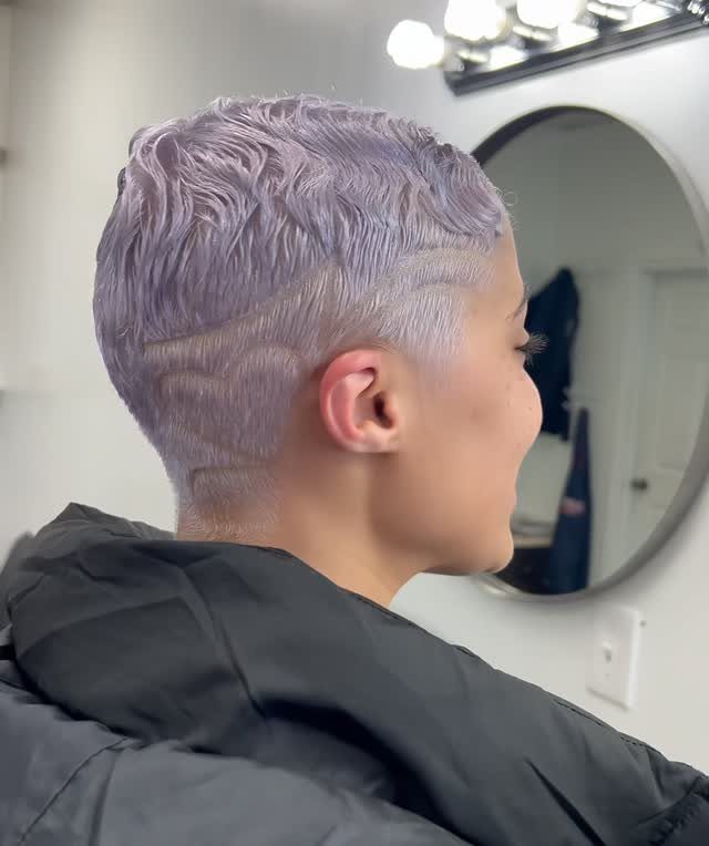 Wavy lavender pixie haircut with closely shaved sides in a salon