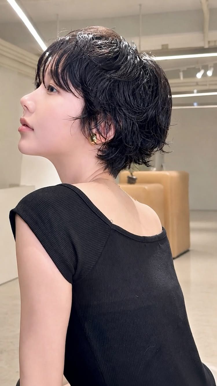 Woman with a glossy, tousled black pixie haircut and bangs in a salon