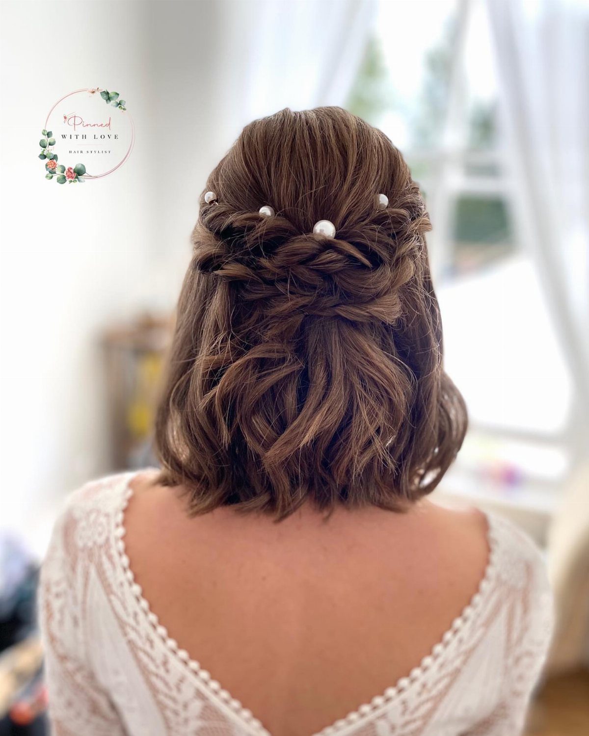 Brown shoulder-length curls twisted and pinned with pearls above a white lace top