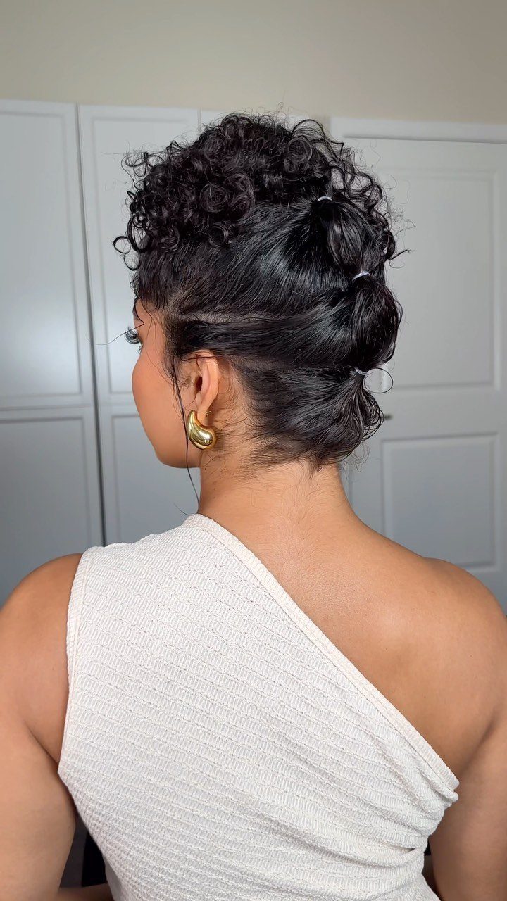 Dark curly hair pinned into a high, textured updo on a woman