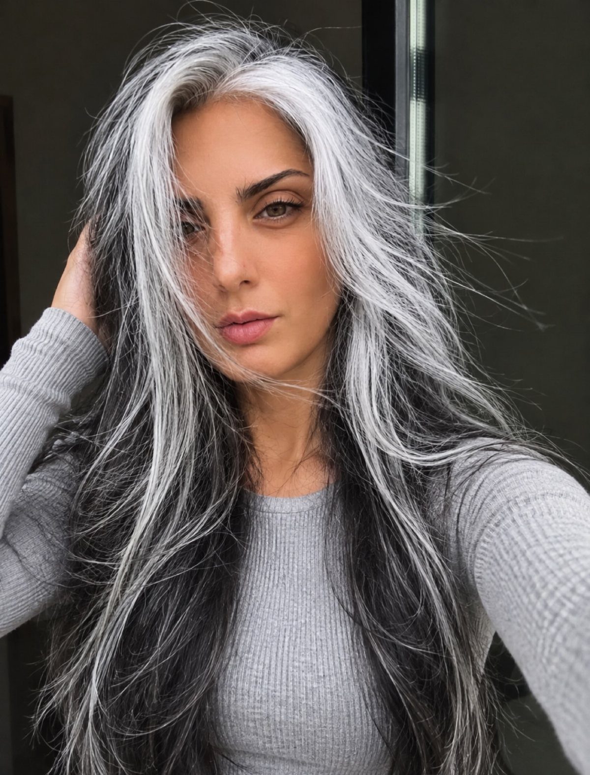 Woman with long icy silver-white waves, dark roots, and a near-middle part