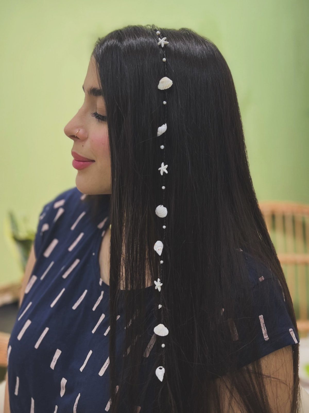 Woman with long black hair and white pearl pieces tracing her center part