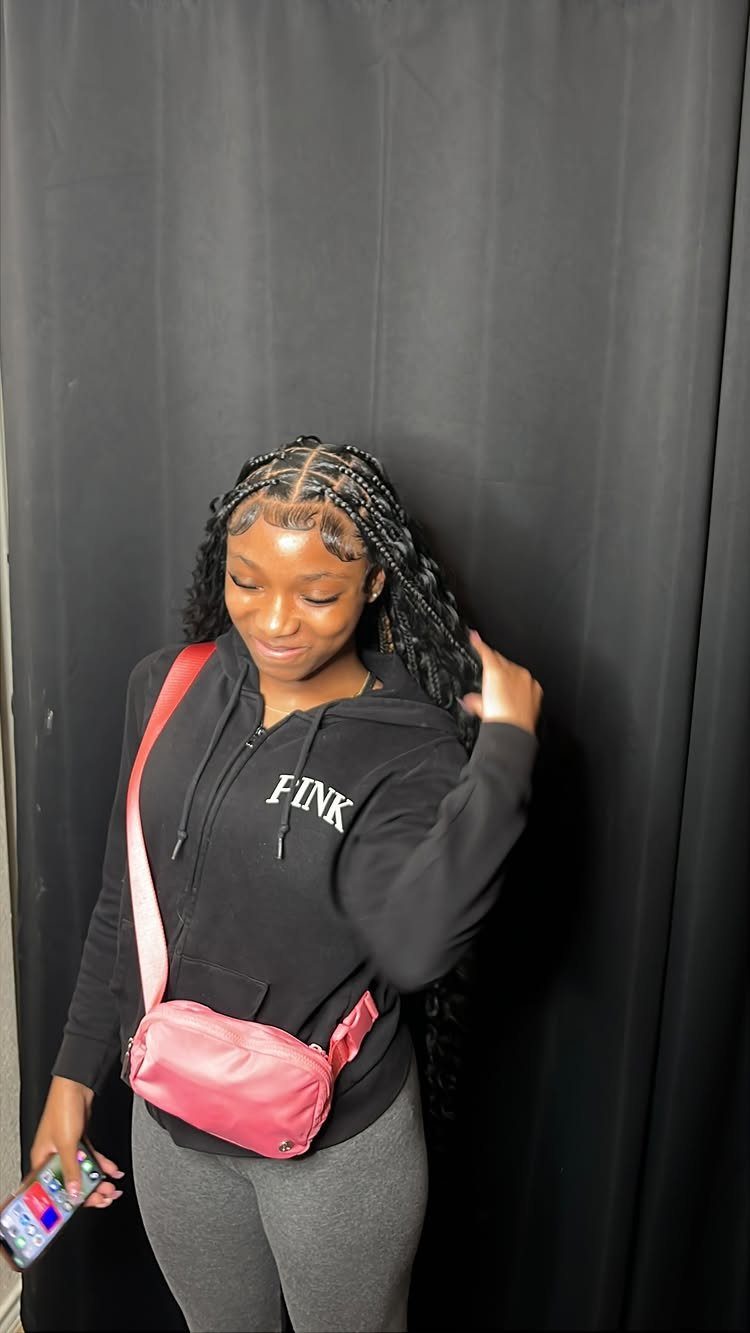 Woman with long textured braids parted near the middle poses in front of a dark curtain
