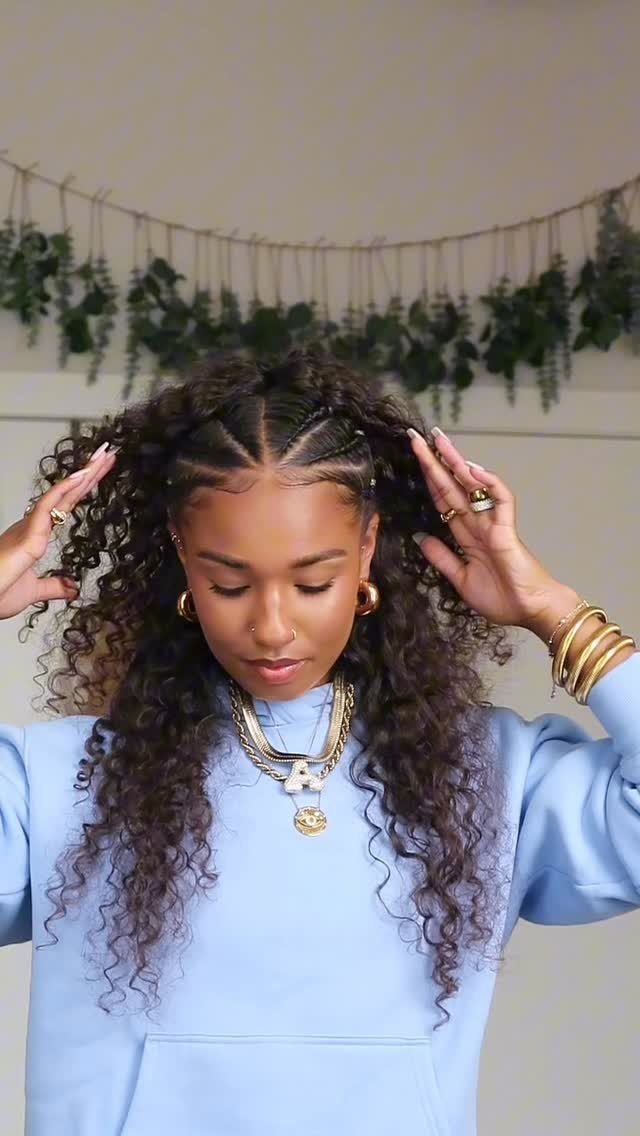 Woman adjusting textured middle-part curls with small braids along the sides