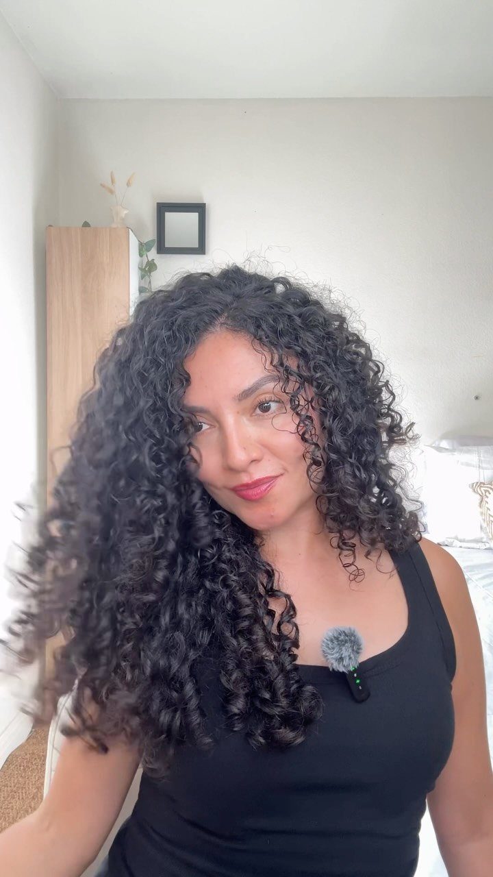 Woman with long dark curls wears a near-middle part and black sleeveless top
