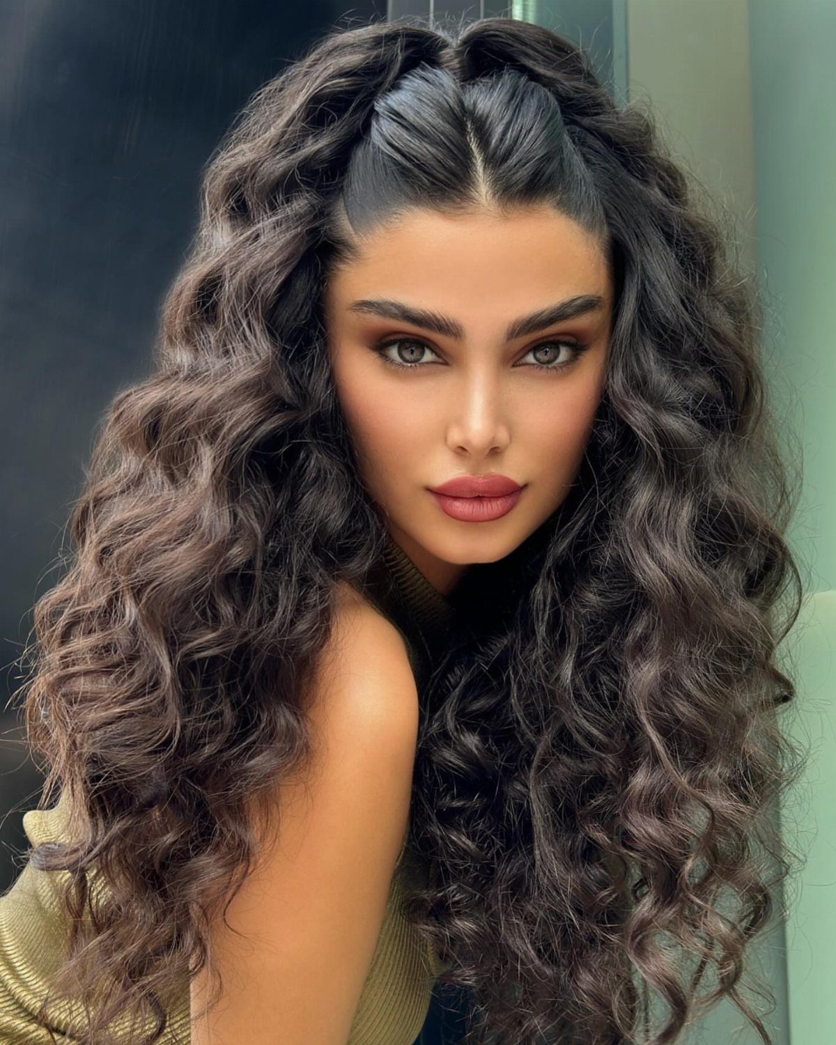Woman with slicked center part and long dark curls cascading over her shoulders