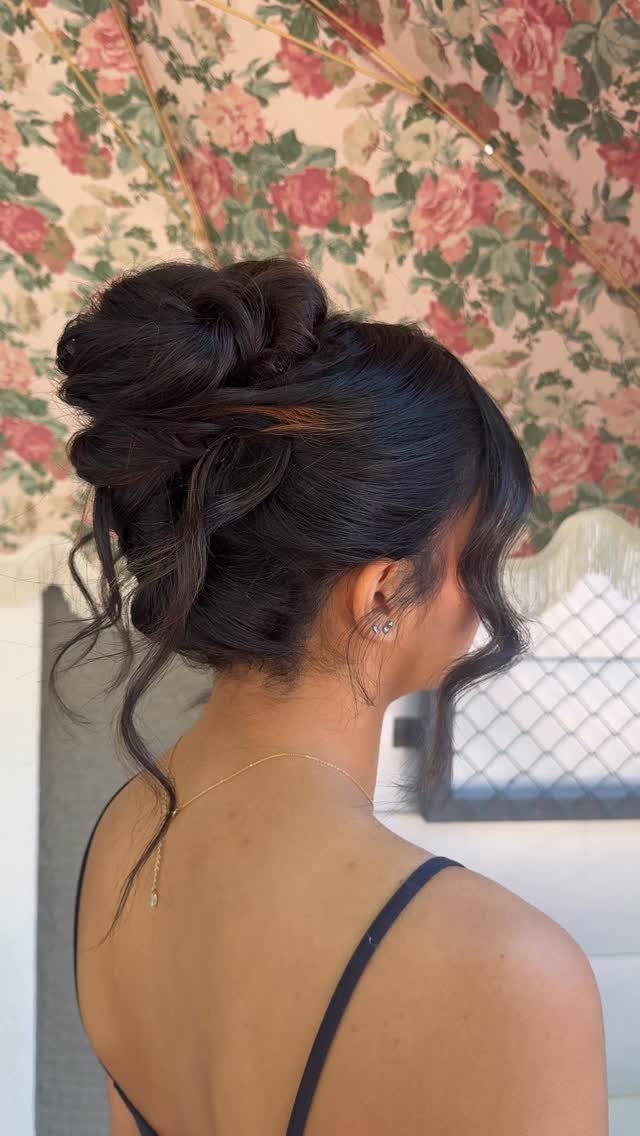 Dark-haired person wears a loose updo with curls framing the face