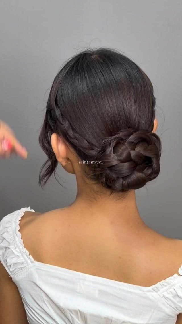 Dark medium hair arranged in a thick braided low bun, viewed from behind