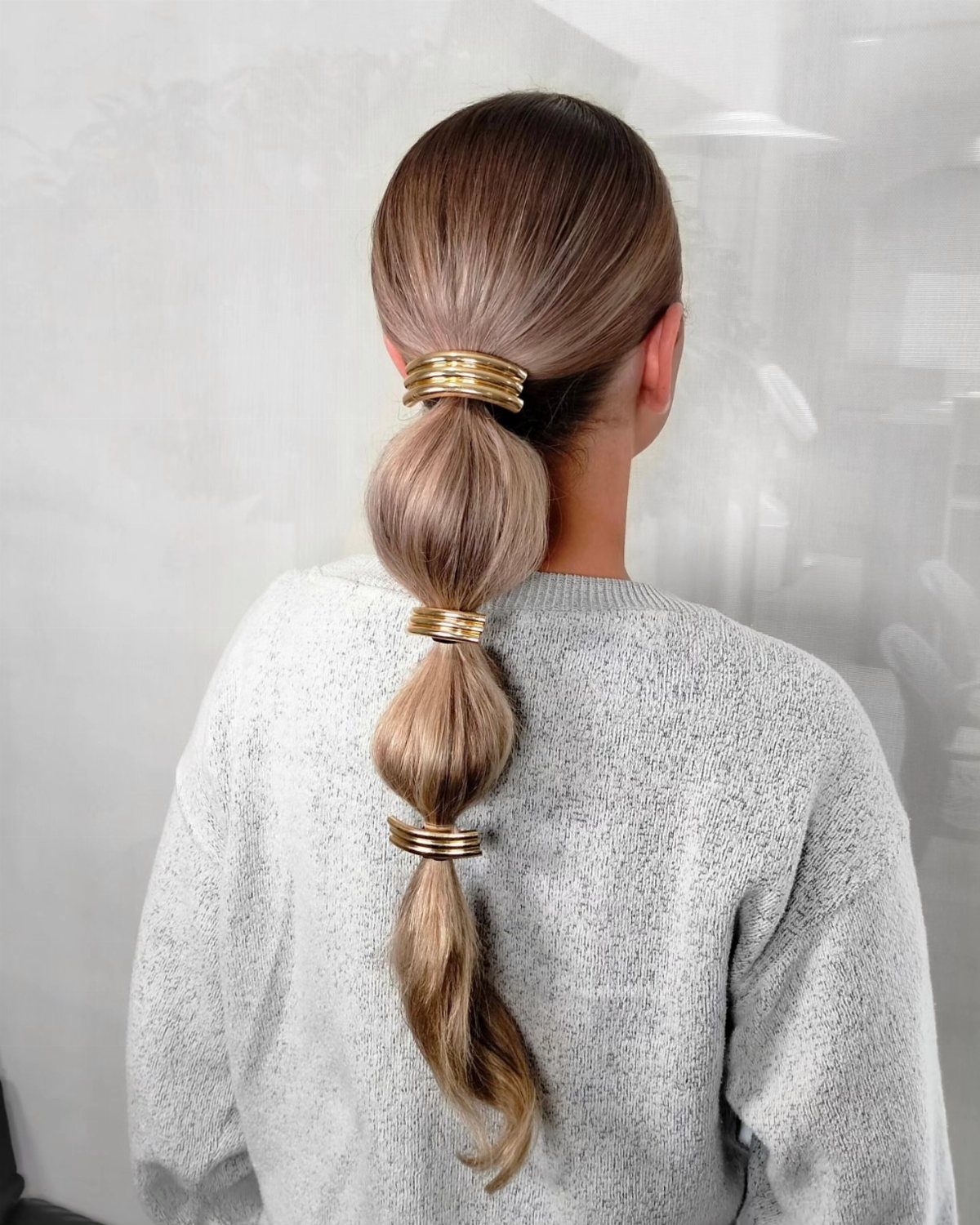 Bubble ponytail with rounded sections and gold cuffs on long light brown hair